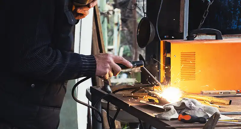 Close-up of a welder's essential PPE including auto-darkening helmet, gloves, and flame-resistant jacket.