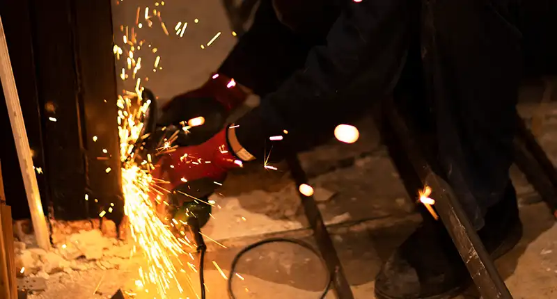 Worker using an overhead crane to safely maneuver a large metal fabrication piece.