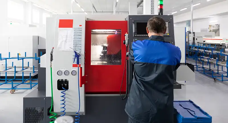 A collaborative robot (cobot) precisely loading a part into a CNC milling machine. Shows human-robot collaboration.